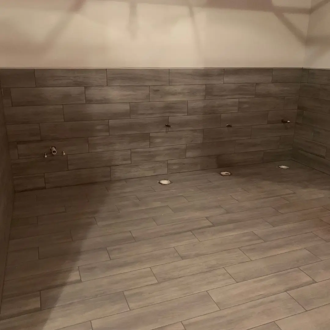 Gray wood-look porcelain tile on the floor and continuing up the restroom walls as wainscot at Treatt USA