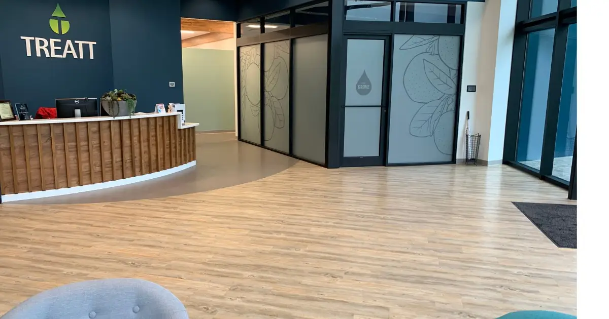 Treatt USA reception area in Lakeland, FL with light wood-look luxury vinyl plank flooring and a wood-clad welcome desk under the Treatt logo