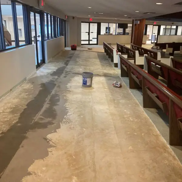 Sanctuary aisle at Winter Haven Nazarene Church stripped down to the bare concrete subfloor with pews pushed aside, ready for new LVP